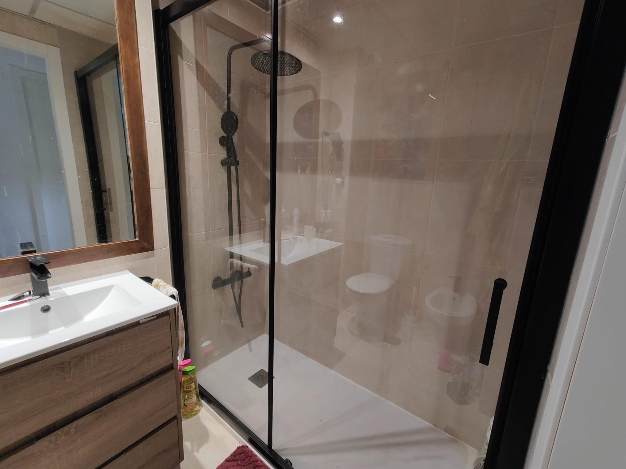 El mismo espacio con plato de ducha a ras de suelo, mampara de perfil negro y mueble de lavabo nuevo